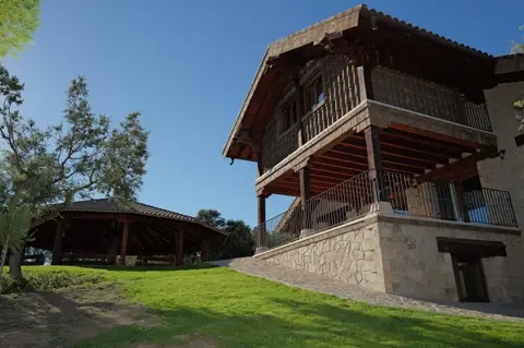 La casa con su balcón de madera y el cenador al fondo
